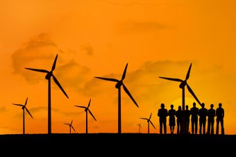 digital composite of silhouette of group of people with windmills on orange sky background